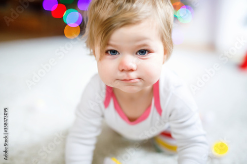 Gorgeous cute beautiful little baby girl playing with educational toys at home or nursery. Happy healthy child learning crawling and standing.
