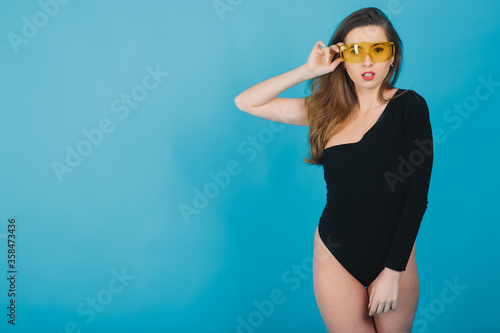 beautiful sporty girl dressed in black bodysuit with yellow glasses on blue background