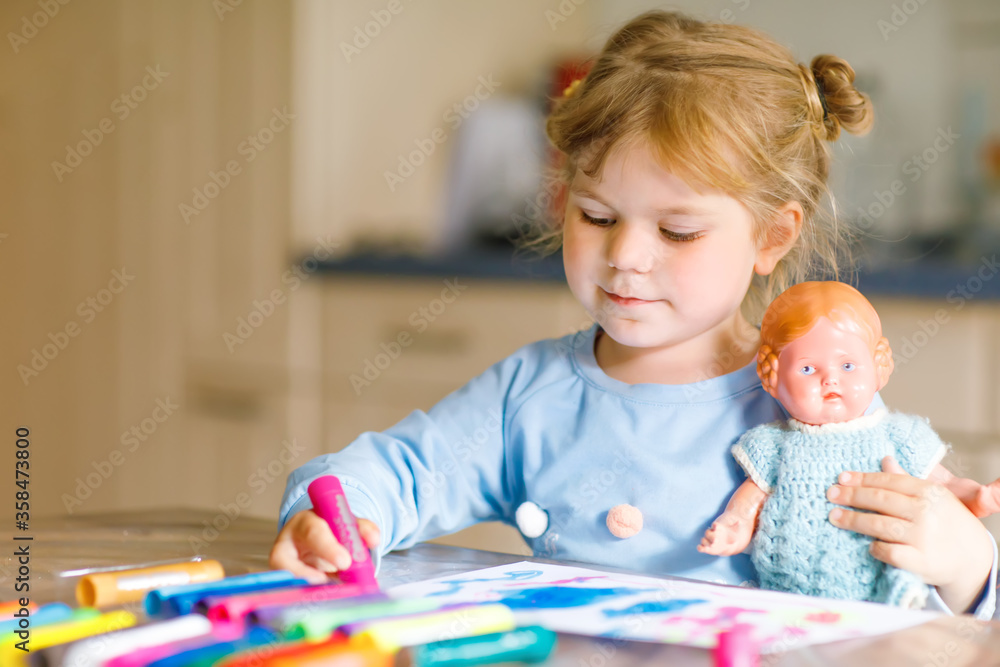 Fototapeta premium little alone toddler girl painting with felt pens during pandemic coronavirus quarantine disease. Happy creative child with old vintage doll, homeschooling and home daycare with parents