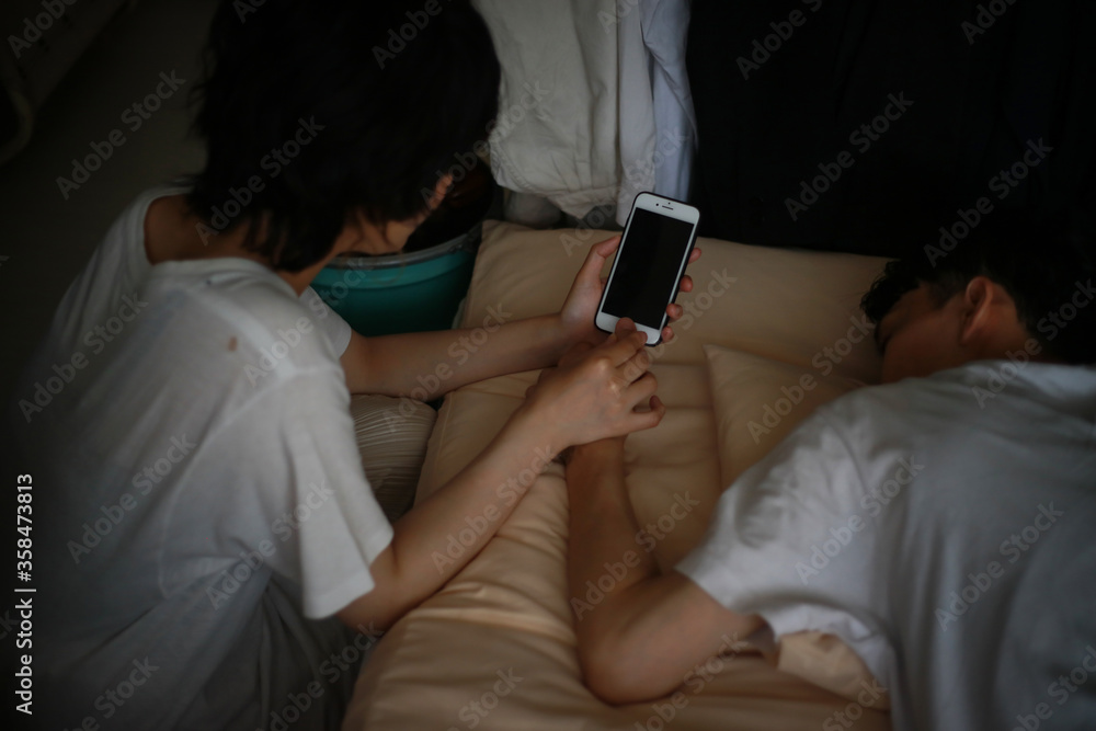 Obraz premium 寝ている男性の指でスマートフォンの指紋認証を解除する女性