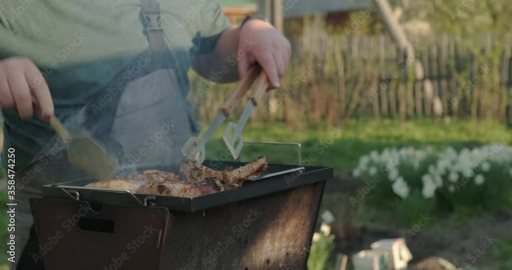 Man Cooking Chicken Steaks On Grill. Cook Prepares Meat for Whole Family. Checks Meat Readiness. Culinary Tongs Turns Meat. Smoke from Hot Coals Rises to Top. Backyard. Rest at Nature. Roast Meat