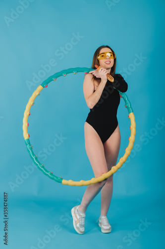 beautiful woman in yellow glasses with a hula hoop holds a hot dog in her hand on a blue background