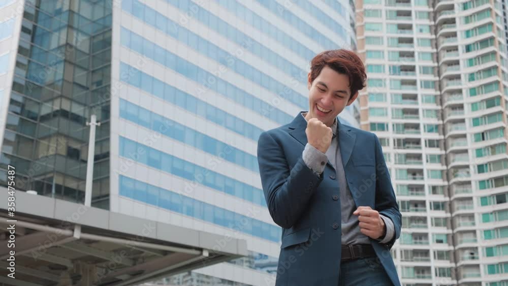 Business win. Businessman look at the camera shaking fists celebrating success at work with modern office building background. business success, achievement, and win concepts Business win. Businessman look at the camera shaking fists celebrating success at work with modern office building background. business success, achievement, and win concepts
