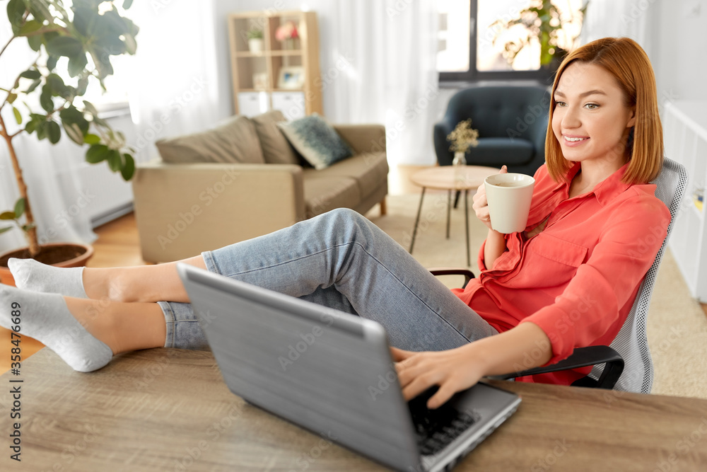 remote job, technology and people concept - happy smiling young woman with laptop computer drinking coffee at home office and resting her feet on table remote job, technology and people concept - happy smiling young woman with laptop computer drinking coffee at home office and resting her feet on table