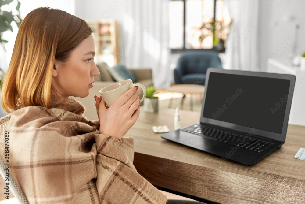 healthcare, technology and people concept - sick young woman in blanket drinking tea and having video call on laptop computer at home healthcare, technology and people concept - sick young woman in blanket drinking tea and having video call on laptop computer at home
