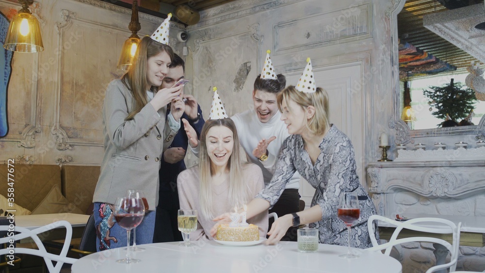 Excited pretty woman blowing birthday candles while dearest friends throwing surprise party