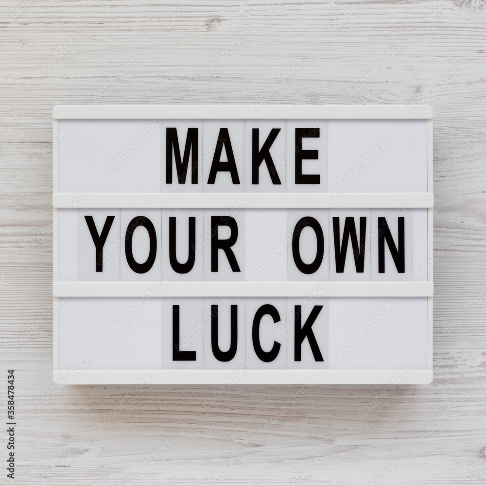 'Make your own luck' on a lightbox on a white wooden surface, top view. Flat lay, from above, overhead. Close-up.