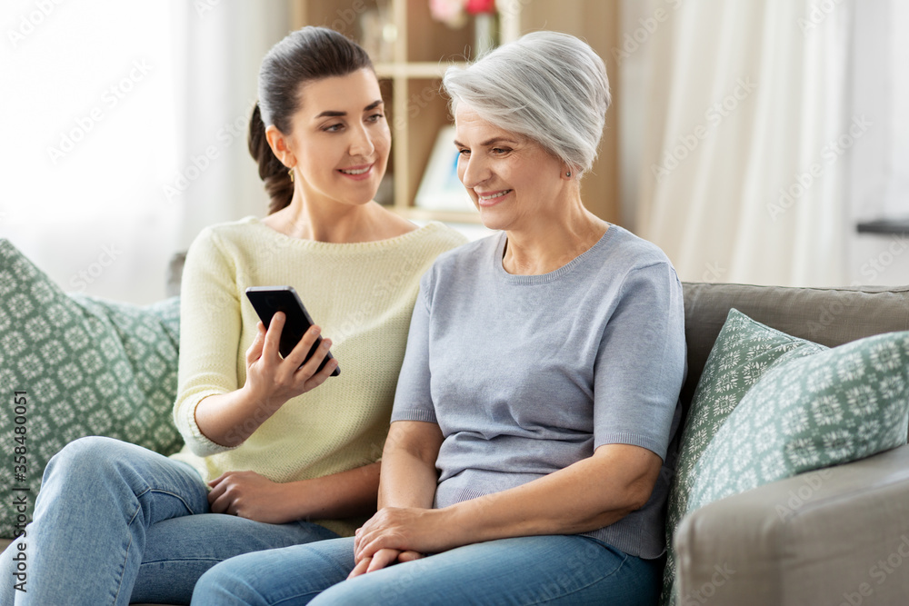 family, generation and technology concept - happy smiling senior mother and adult daughter with smartphone at home family, generation and technology concept - happy smiling senior mother and adult daughter with smartphone at home