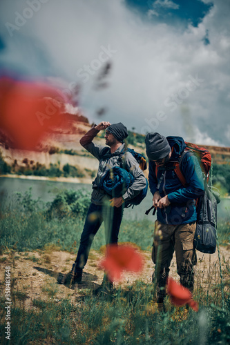 Two handsome men with backpacks on standing in beautiful nature and searching a good place for tent. Camping on weekend concept.