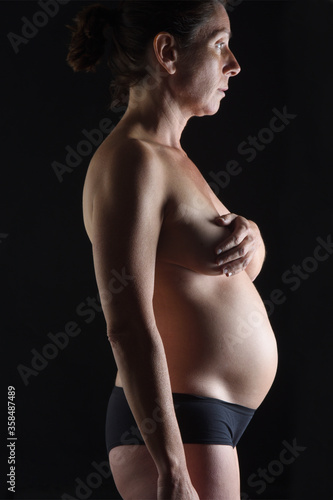 portrait of pregnant woman naked on black background, six months;