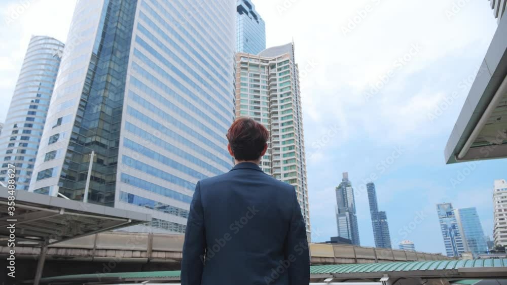 Back view of the Thoughtful Businessman wearing a Suit looking out while standing near modern Office Building background. 4K Slow Motion Corporate. Back view of the Thoughtful Businessman wearing a Suit looking out while standing near modern Office Building background. 4K Slow Motion Corporate.