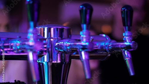 Equipment for production, bottling and cooling the beer and other beverages in bar or restaurant. Beer tap on colorful night party. Multi-colored lights of party