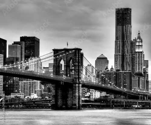 A black and white square crop of the Brooklyn Bridge at night.