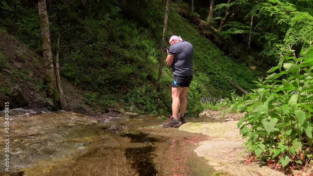 photographer hiker taking photos of waterfall and rocks with the camera, deep into mountains photographer hiker taking photos of waterfall and rocks with the camera, deep into mountains