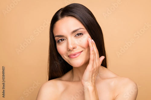 Closeup photo of naked latin lady model natural beauty without makeup touch cheek pure soft smooth skin applying anti age cream isolated beige pastel color background photo