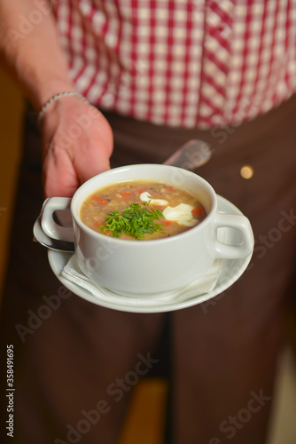 A waiter wearing plaid uniform serving a bowl of hot soup in a restaurant. Concept for a tasty and healthy meal.