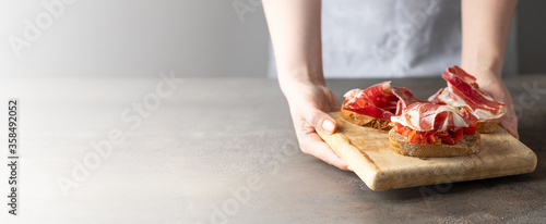 Fotografie, Tablou Woman holding wooden try with toasted brad slice with fresh tomatoes and cured ham