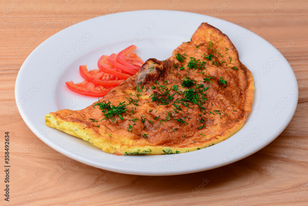 Delicious egg omelette with greens and tomatoes. Served on a white plate over light rustic wooden table background.