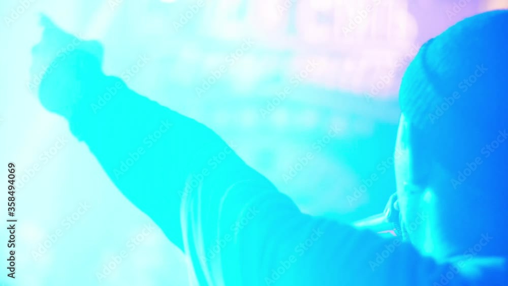 Russia, St. Petersburg - June 2020. Close-up of a young guy with a microphone on a nightclub stage. Multi-colored lights of party on the dance floor of a night club. Skillful DJ performing at a club.