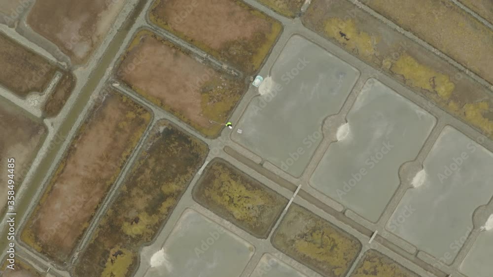 A Salt Worker Raking Saline In A Salt Evaporation Pond In Guerande, France - aerial drone A Salt Worker Raking Saline In A Salt Evaporation Pond In Guerande, France - aerial drone