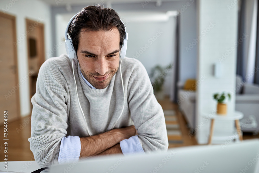 Smiling entrepreneur with headphones surfing the net on laptop at home.