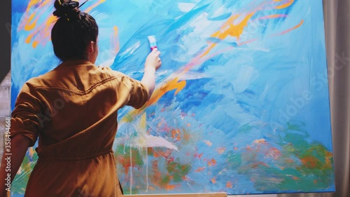 Innovative female painter using orange paint on big canvas. Modern artwork paint on canvas, creative, contemporary and successful fine art artist drawing masterpiece