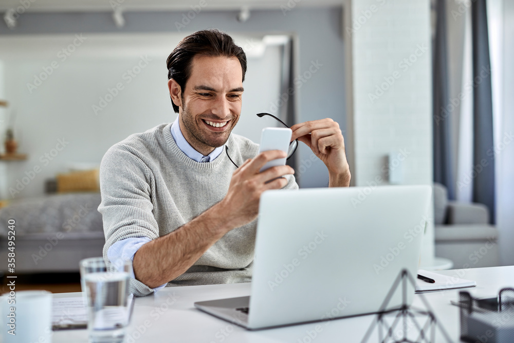 Happy entrepreneur texting on mobile phone while working at home. Happy entrepreneur texting on mobile phone while working at home.