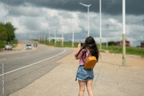 a girl with long hair in a pink T-shirt stands near the road and takes pictures on the phone