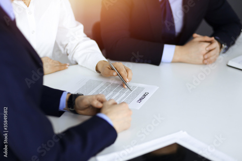 Group of business people, men and a woman, discuss details of a contract at meeting in a sunny modern office. Discussion at negotiation or workplace. Teamwork, partnership and business concept
