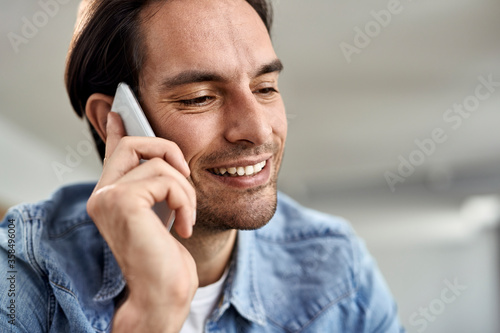 Young happy man using smart phone while making a phone call at home.