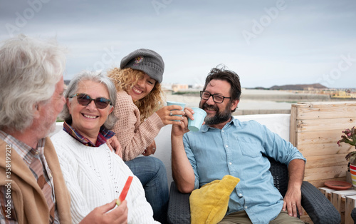 Four happy people together, senior and middle-aged people having fun eating and drinking outdoors on the terrace - couples different generations and the same love concept