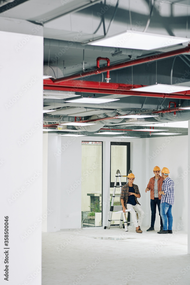 Long shot of three professional construction workers spending time in unfinished room having lively discussion, copy space Long shot of three professional construction workers spending time in unfinished room having lively discussion, copy space