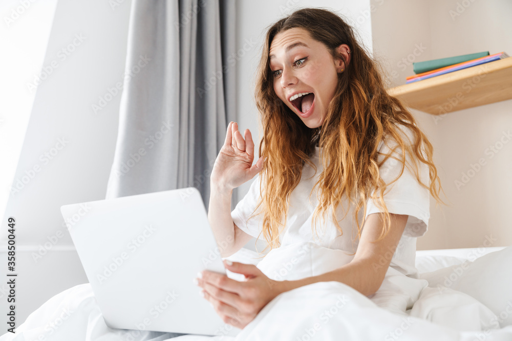 Portrait of woman waving hand and using laptop while sitting in bed Portrait of woman waving hand and using laptop while sitting in bed