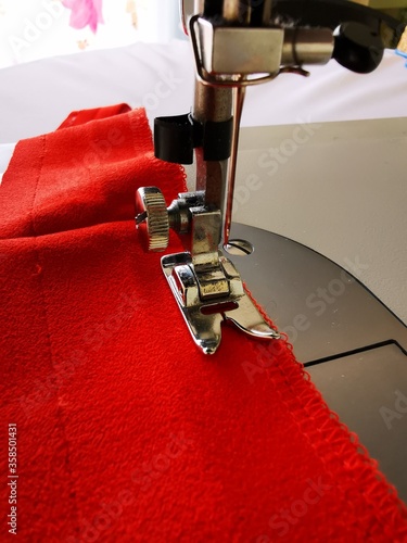 Fototapeta Red fabric being sewed by a sewing machine