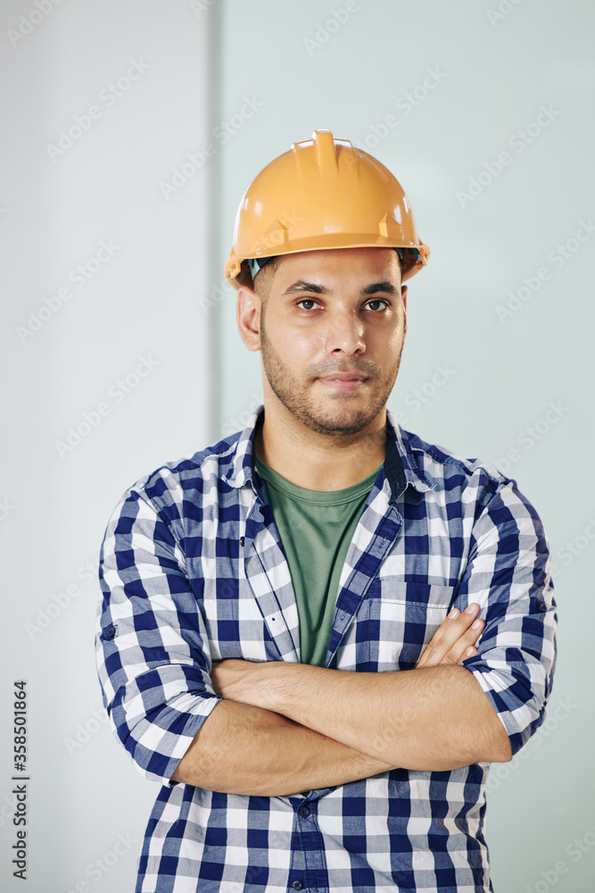 Waist up portrait shot of modern construction worker wearing checked shirt and protective hardhat standing with arms crossed Waist up portrait shot of modern construction worker wearing checked shirt and protective hardhat standing with arms crossed