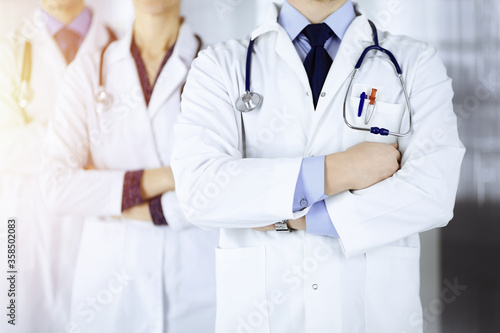 Group of modern doctors standing as a team with crossed arms and stethoscopes in a sunny hospital office. Physicians ready to examine and help patients. Medical help, insurance in health care, best