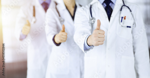 Group of unknown doctors stand as a team with thumbs up in a sunny hospital office. Physicians ready to examine and help patients. Medical help, insurance in health care, best desease treatment and