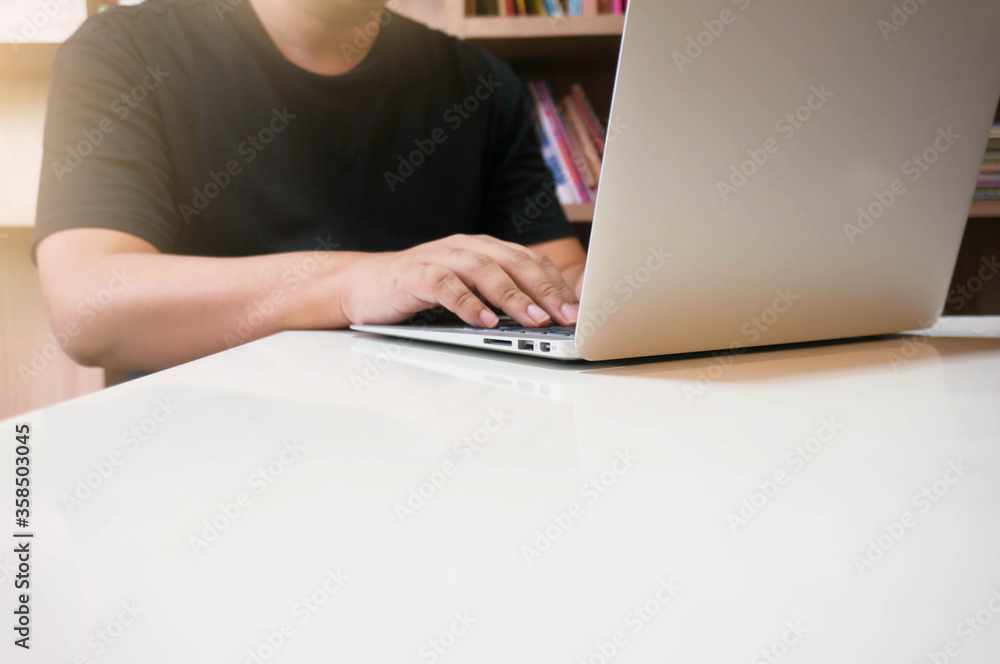 Fototapeta premium image of a young man working on his laptop in library, rear view of business man hands busy using laptop at office desk, young male student typing on computer sitting at wooden table