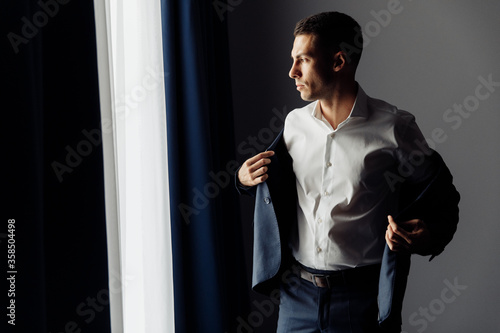 Handsome brutal groom in blue suit near the window 