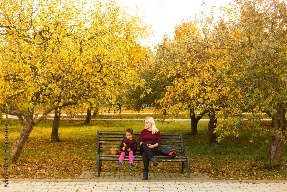 Happy mother and daughter embracing on a bench in an autumn park Happy mother and daughter embracing on a bench in an autumn park