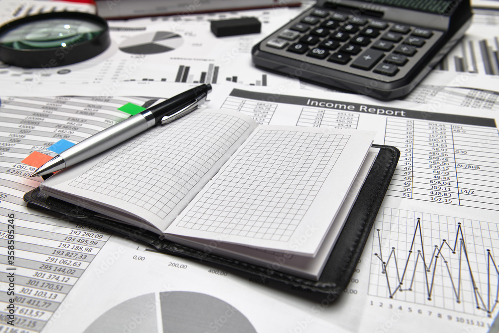 Top view of office employee's desk - work with financial reports, analysis and accounting, tables and graphs, various office items for bookkeeping Top view of office employee's desk - work with financial reports, analysis and accounting, tables and graphs, various office items for bookkeeping