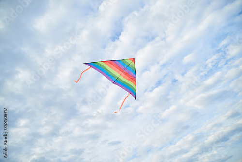 Young brunette woman, wearing casual clothes green t-shirt, playing with colorful kite on green field meadow in summer, running, jumping. Family leisure activity at natural rural landscape.