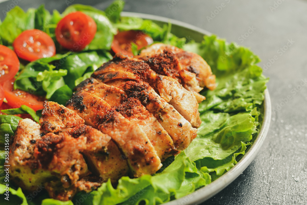 Grilled chicken breast salad with spinach and tomatoes. Healthy eating Fried chicken breast, lemon, cherry tomatoes, spinach and lettuce. Dark background. Close up.