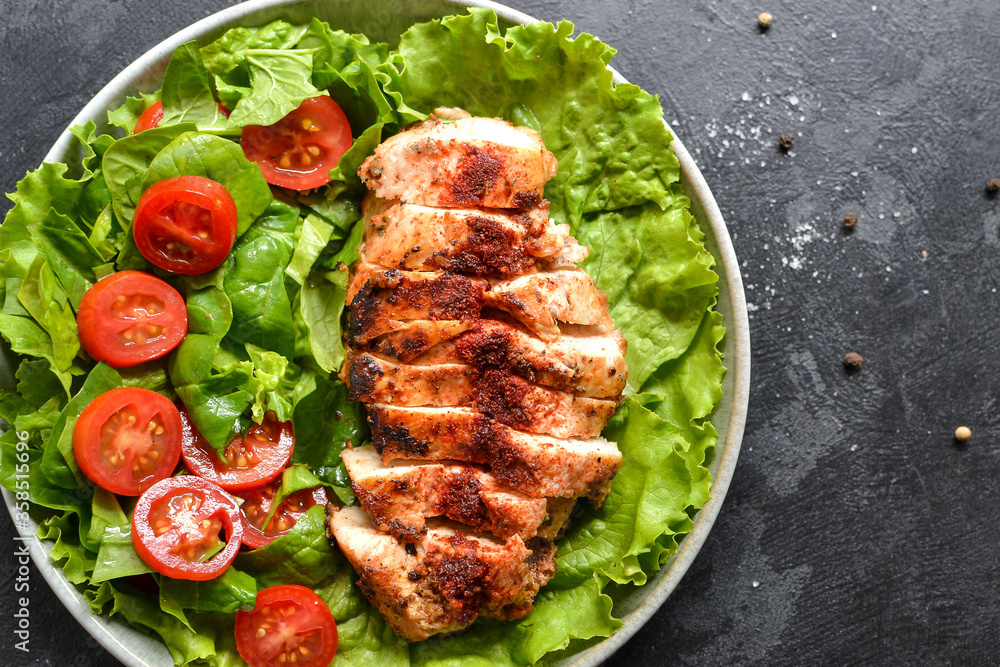 Grilled chicken breast salad with spinach and tomatoes. Healthy eating Fried chicken breast, lemon, cherry tomatoes, spinach and lettuce. Dark background. Close up.