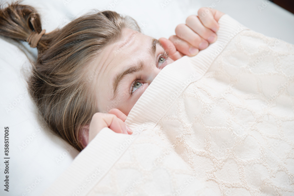 A young attractive man peeks out from under the blankets hiding behind