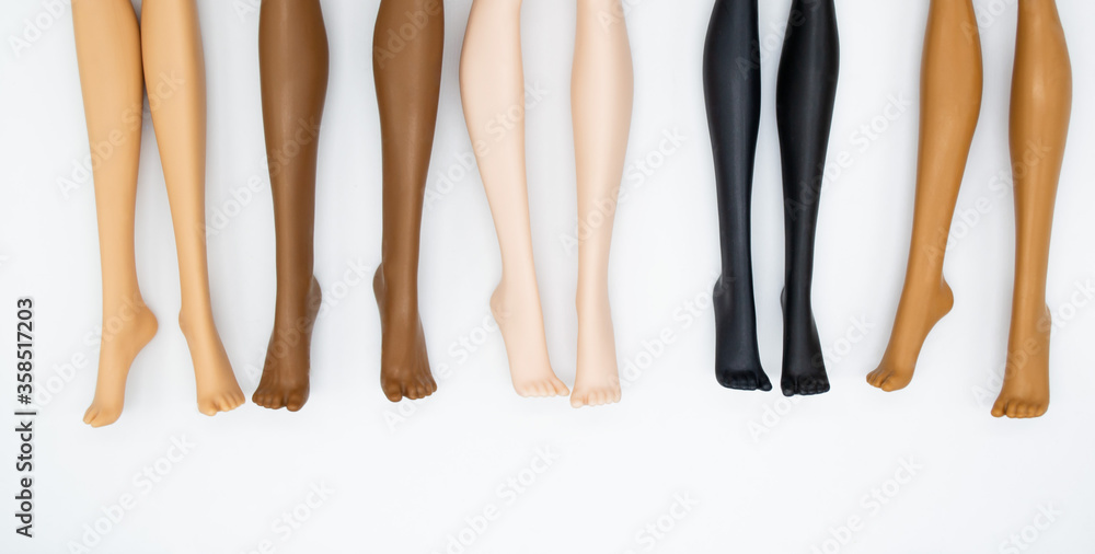 Legs of dolls representing different races on a white background. The concept of female friendship, health, beauty. Space for text Legs of dolls representing different races on a white background. The concept of female friendship, health, beauty. Space for text