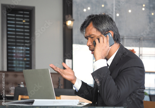 Asian businessman in suit talking on mobile phone in modern office.
