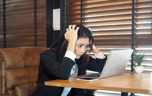 Asian woman sitting in cafe and holding head in hands.Worried businesswoman using laptop in her office and has headache because of problems at work.Stressed businesswoman working on computer.