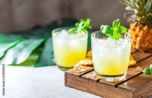 Freshly squeezed pineapple juice with slices of pineapple on a light gray concrete background. Concept of summer healthy fruit drink.