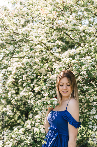 Sensual calm portrait of beautiful hipster woman in blooming bush with white flowers of spirea. Copy space. Stylish blonde woman in blue dress in garden
